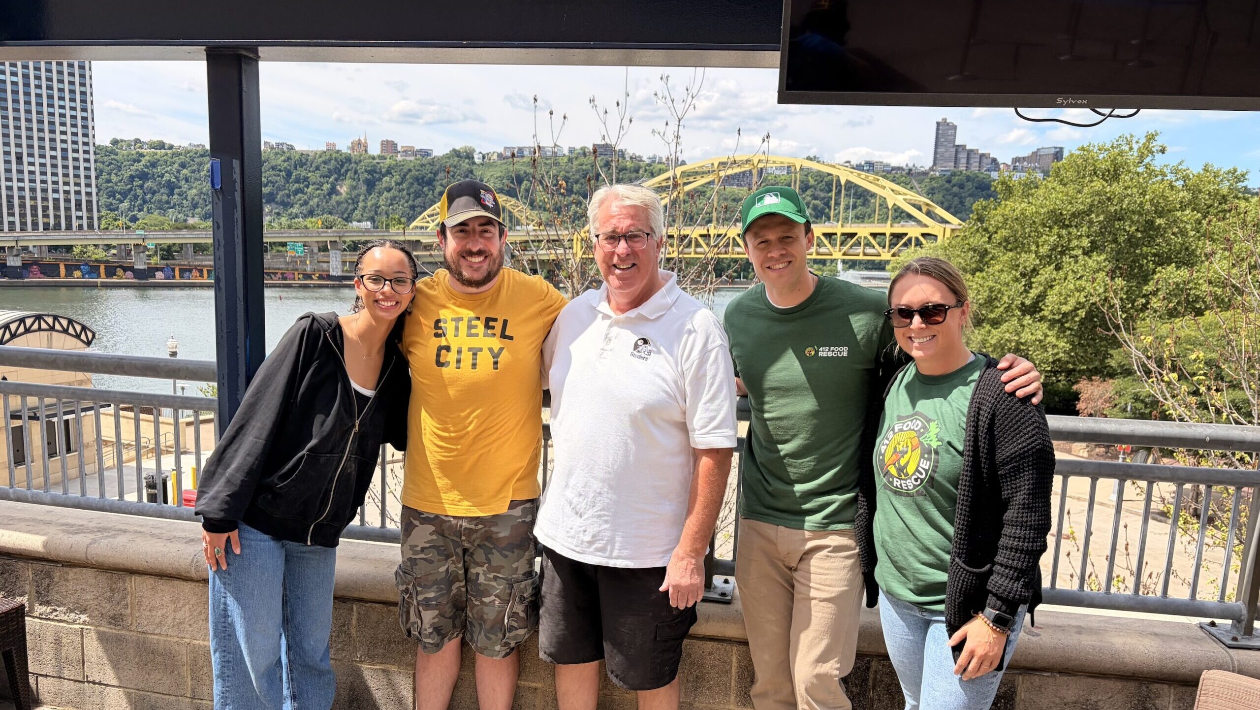 Five people pose closely near a bridge in Pittsburgh.