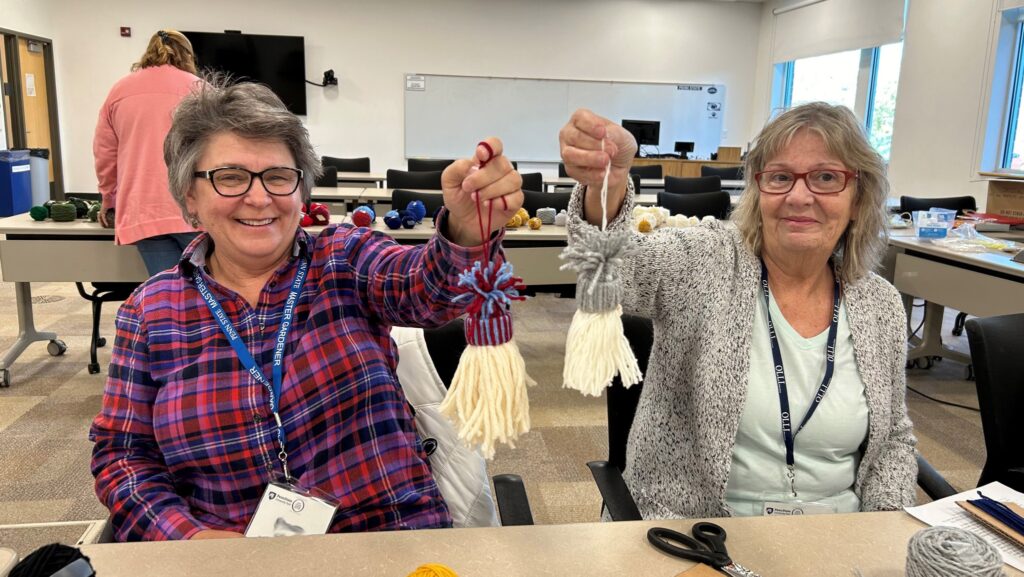 Two female OLLI members holding holiday ornament crafts they made in class