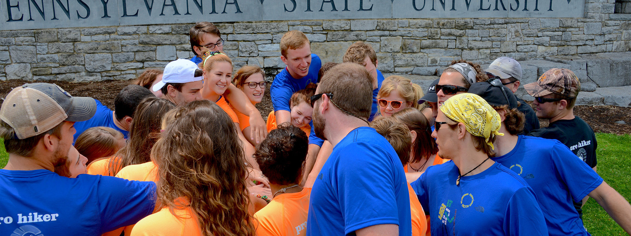 Students with hands in a circle next to The Pennsylvania State University sign