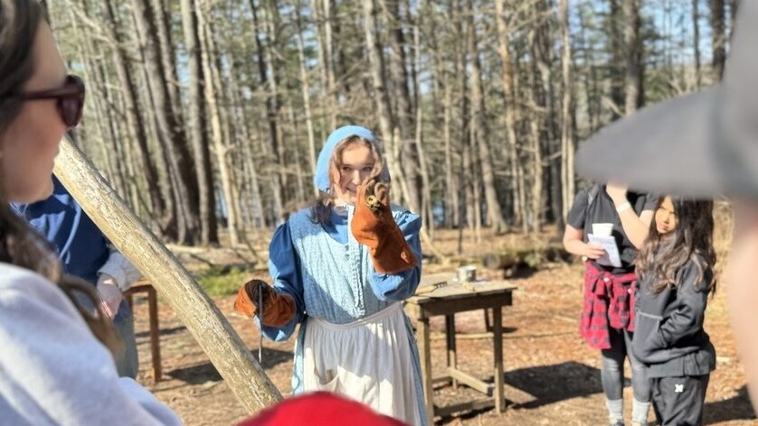 A woman dressed as a pioneer holds up a tool for a crowd.