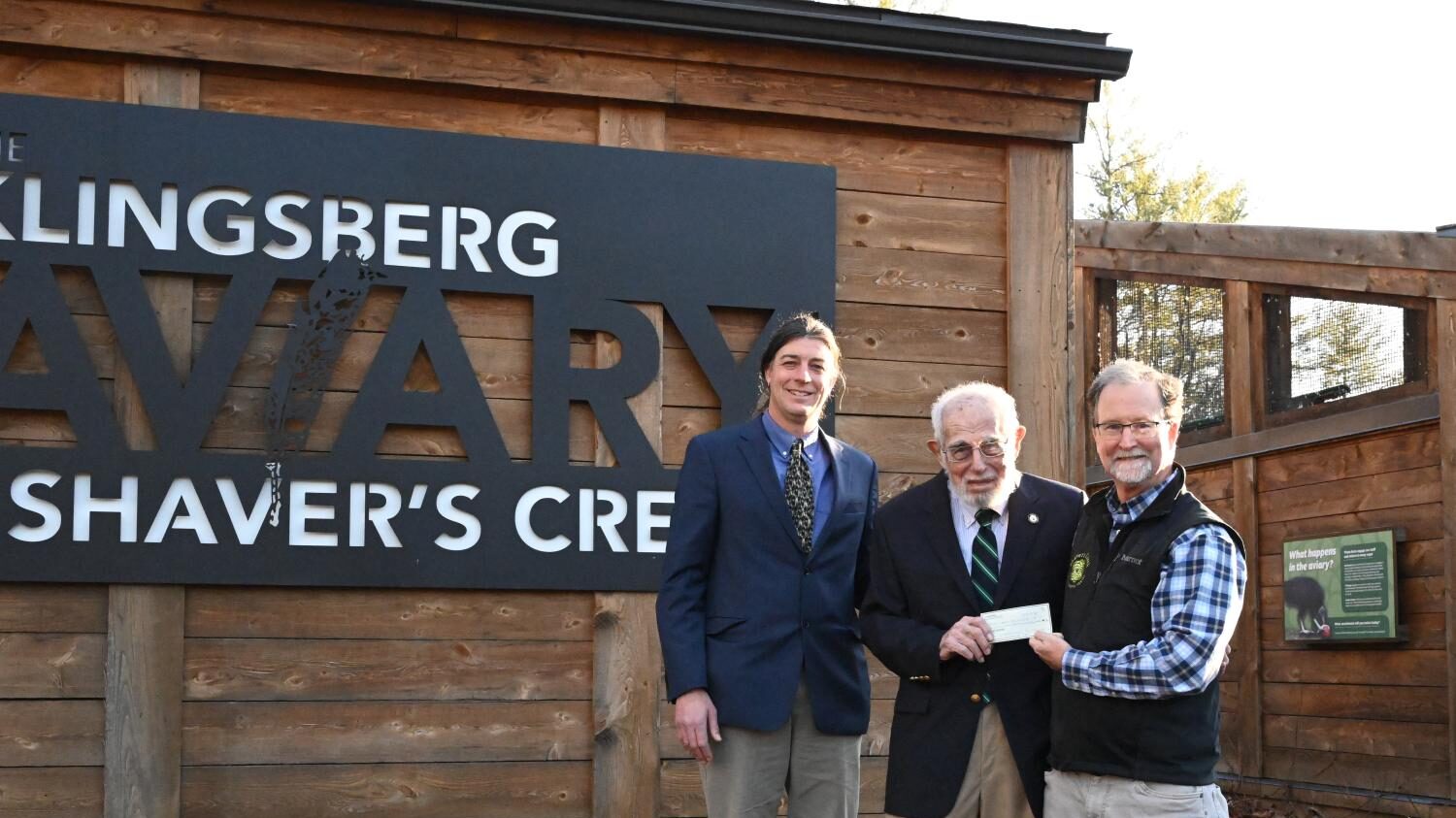 Jason Beale, Cyrus Klingsberg, and Mark McLaughlin pose beside the Klingsberg Aviary sign at Shaver's Creek
