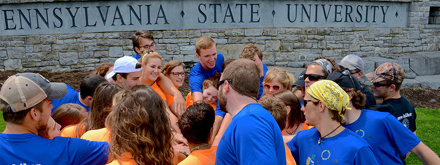 Students with hands in a circle next to The Pennsylvania State University sign