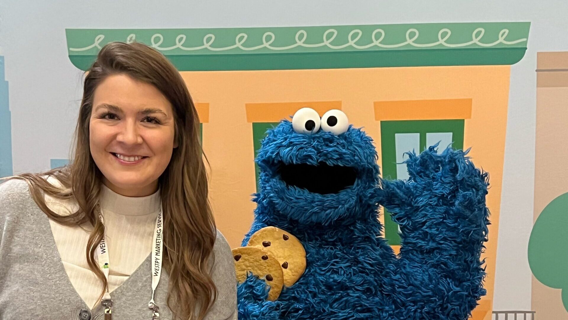 Sydney Forde poses with Cookie Monster, who is holding cookies and waving to the camera